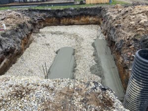 Excavation avec gravier, armatures en acier et coulée de béton frais pour fondations d'une future structure.