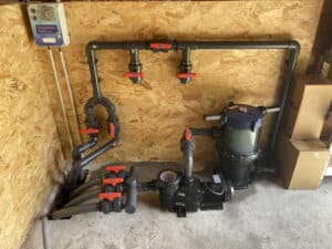 Système de filtration de piscine installé : pompe Hayward, filtre, boîtier de contrôle AstralPool avec minuterie, tuyauterie PVC grise et vannes à bille rouges.