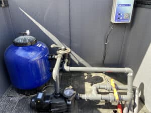 Équipement de filtration de piscine : filtre bleu, pompe Hayward, multi-vannes, et boîtier de commande AstralPool avec minuterie.