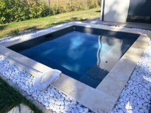 Petit bassin de nage ou piscine rectangulaire moderne, bordée de margelles en pierre claire et de galets blancs, avec filet d'entretien.