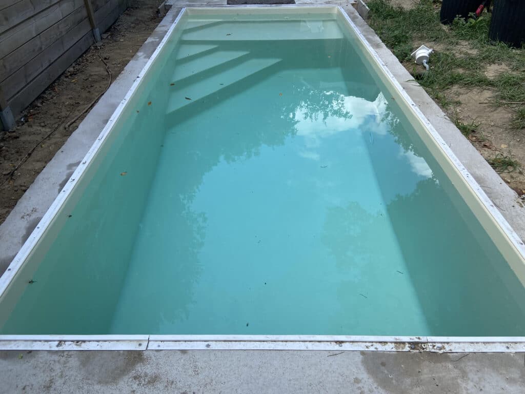 Piscine hors-sol rectangulaire en cours d'installation, remplie d'eau turquoise, avec marches intégrées et margelle en béton.