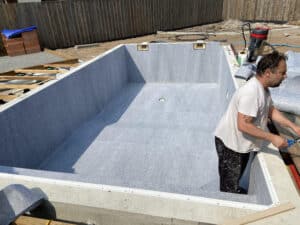 Ouvrier posant une doublure feutrée grise dans une piscine en construction, avec inscription "LIPUISSE 10 GRIS 2025".